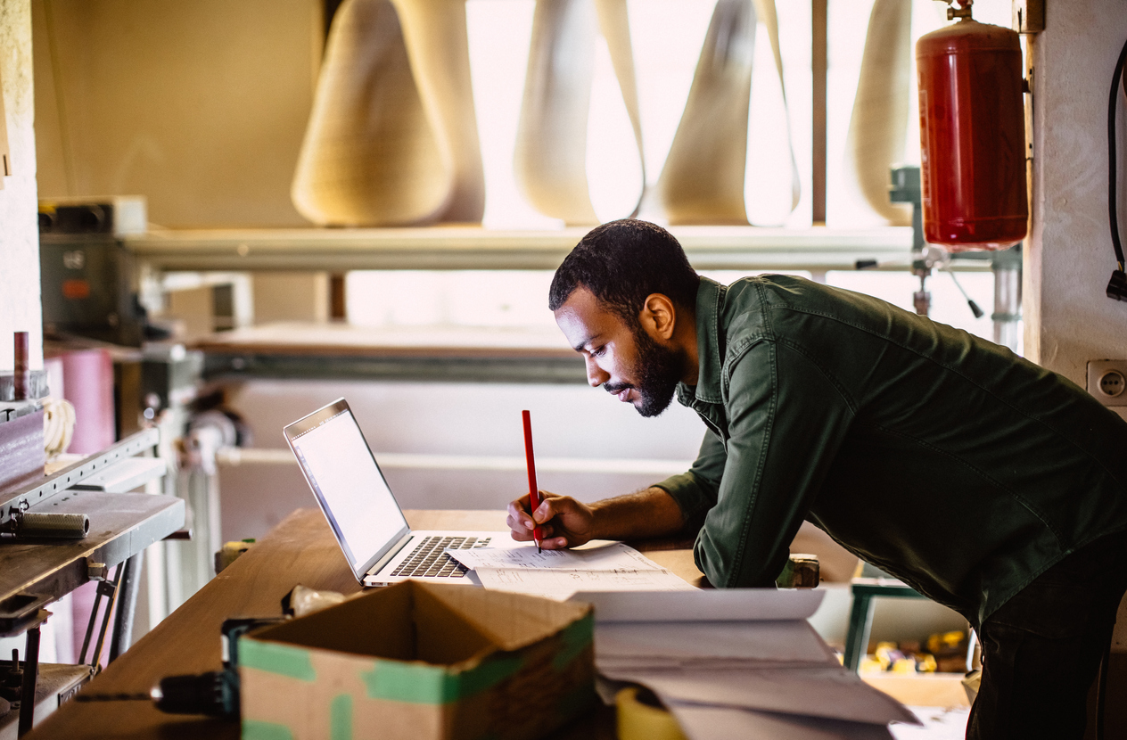 man writing on paper and looking at laptop