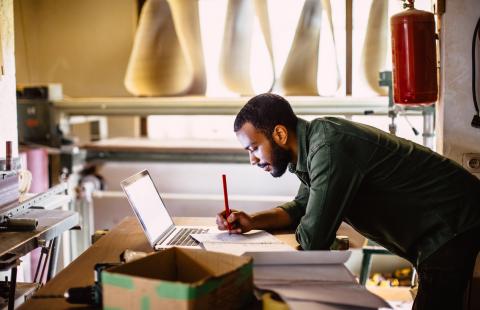 man writing on paper and looking at laptop